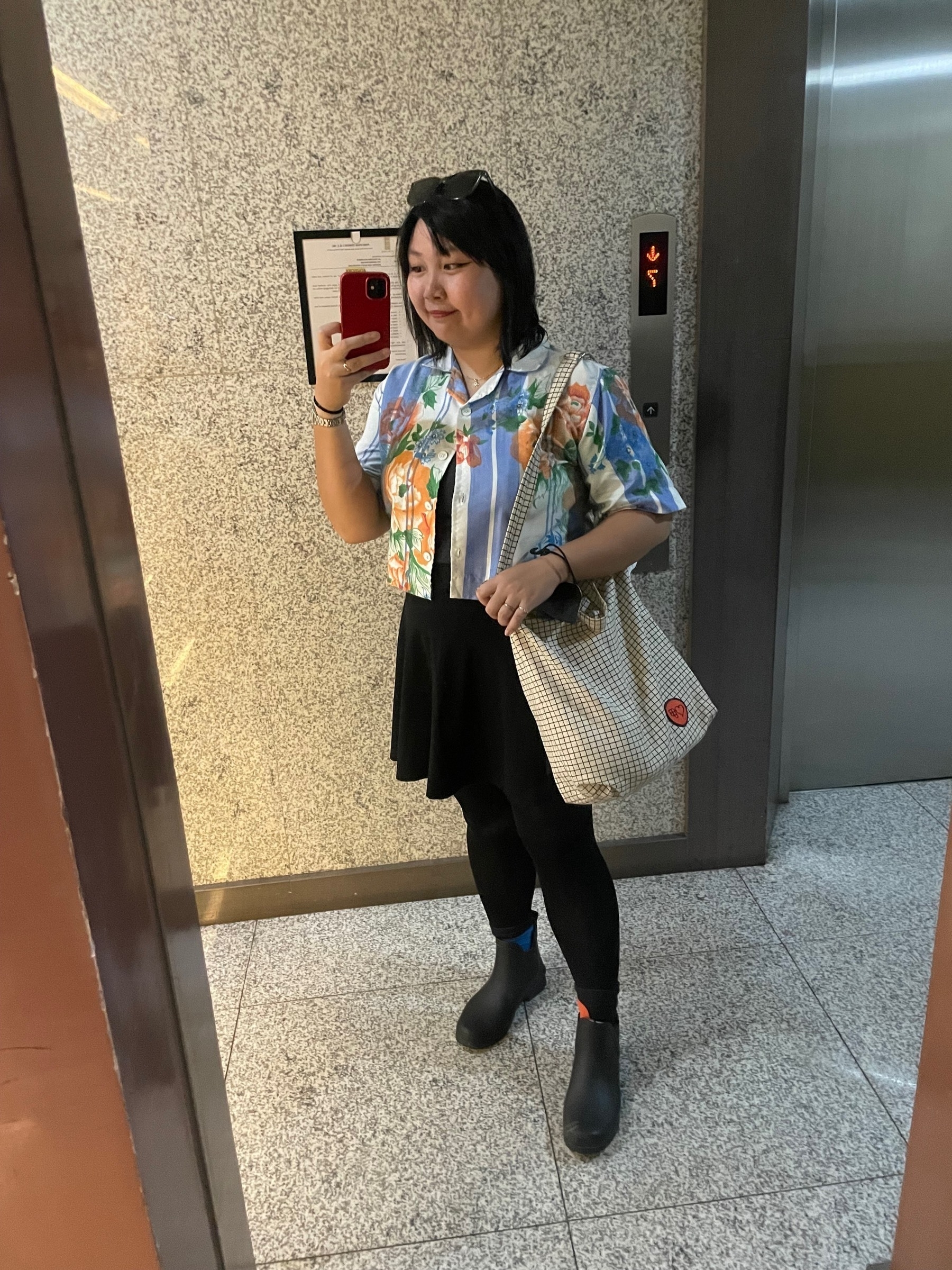 Mirror selfie of Chi wearing a crop top with the pattern of a Filipino blanket, black skater skirt, black leggings, Figma patterned socks and black boots. On her right shoulder is her Friends of Figma black-on-white grid patterned tote bag.