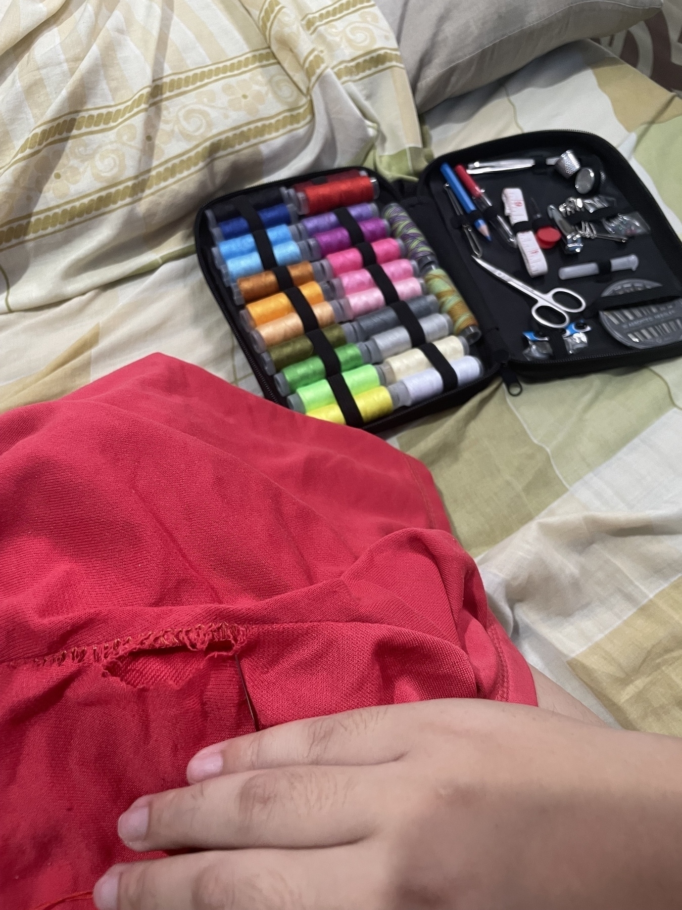 Chi has one of her red shorts with a big hole in it on her lap, and next to her knee is a sewing kit with a bunch of different colored threads and other sewing materials in the black clutch bag.