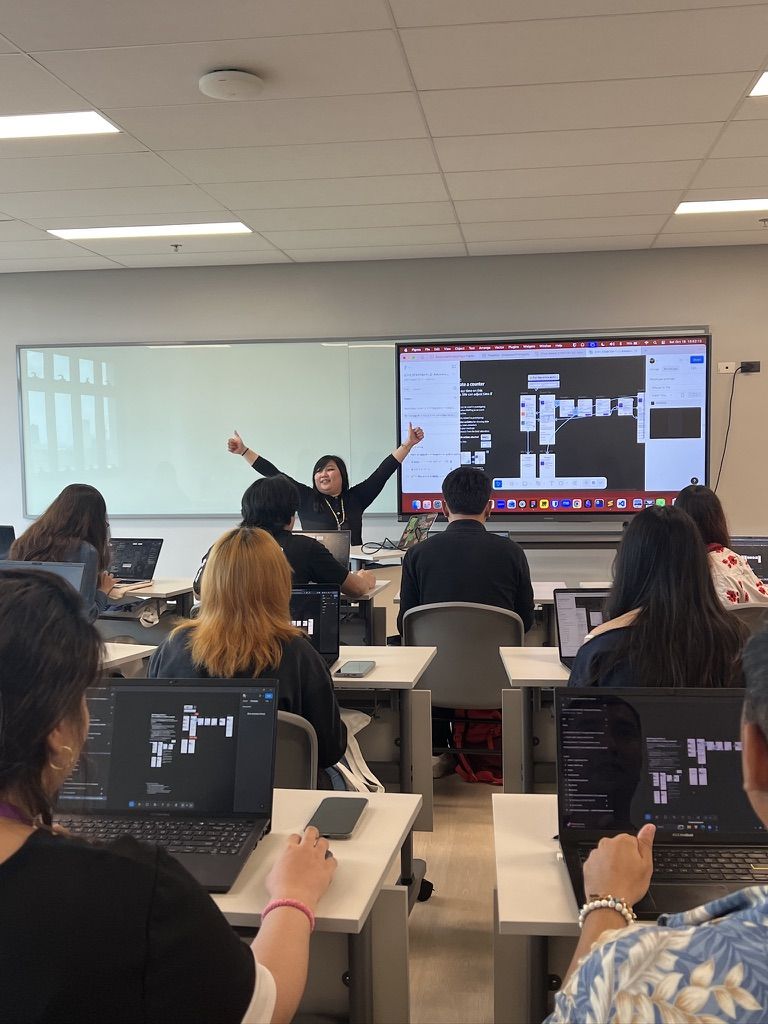 Full house!! Kept trying to make sure everyone could follow along but it was a bit hard ;u; Chi is in front of a classroom, raising both her hands thumbs up and looking around the workshop attendees who are facing her. Attendees all have their laptops open and is seen following along what Chi is also showing on the screen.