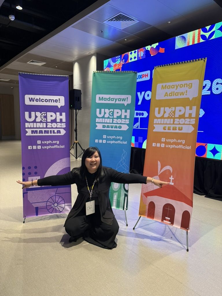 Posing in front of all 3 tarps for UXPH Mini 2025, where the 3 legs are represented Chi posing in front of all 3 tarps for UXPH Mini 2025, with her arms stretched to the sides. The tarps behind her show, from left to right, the one for Manila, Davao, and Cebu legs.