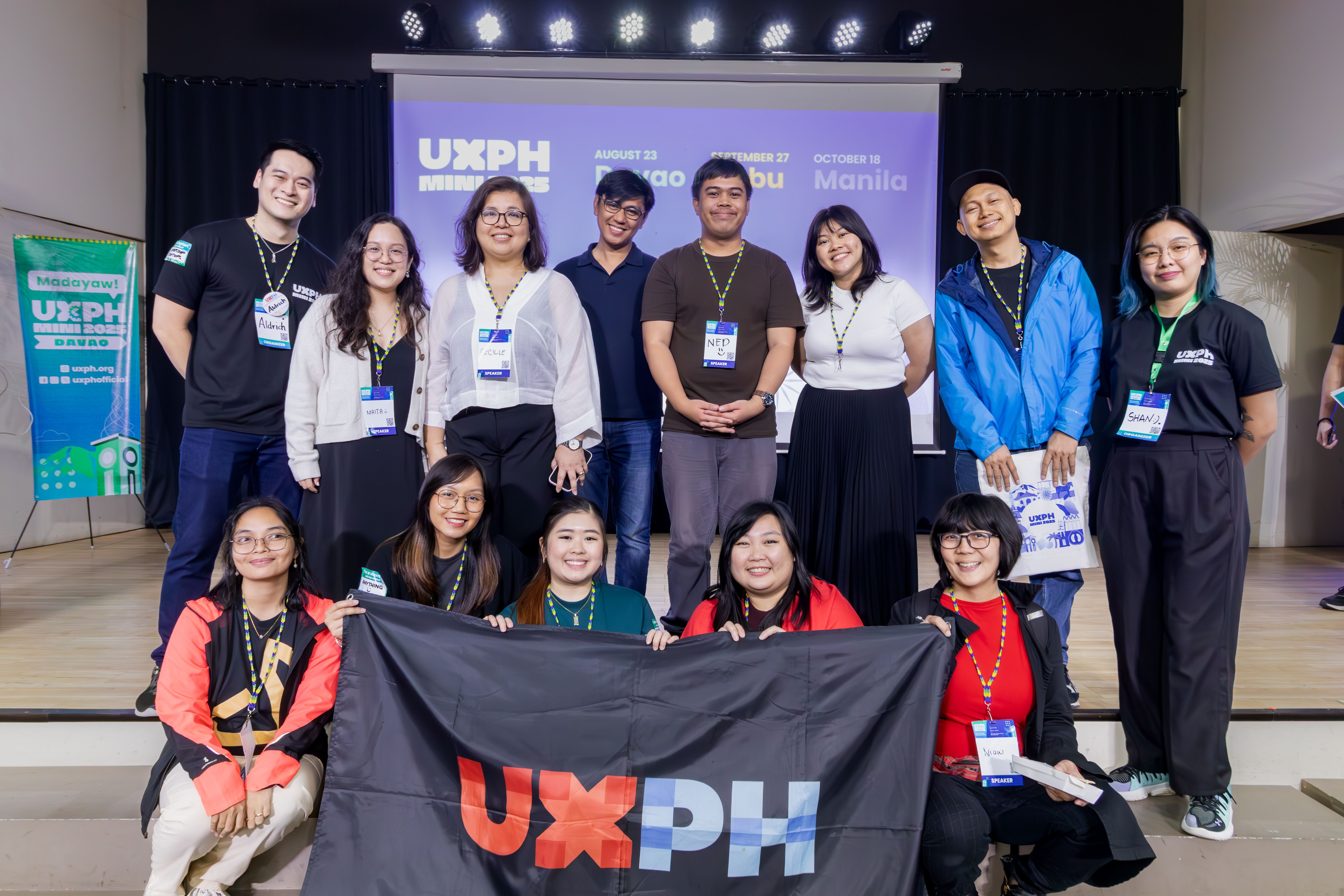 With other speakers and workshop facilitators for UXPH Mini 2025: Davao! 😄 Group photo of the speakers, workshop facilitators, and the main organizers for UXPH Mini 2025: Davao. Chi is seated at the second row, helping hold up a black cloth flag with the UXPH logo printed on it.