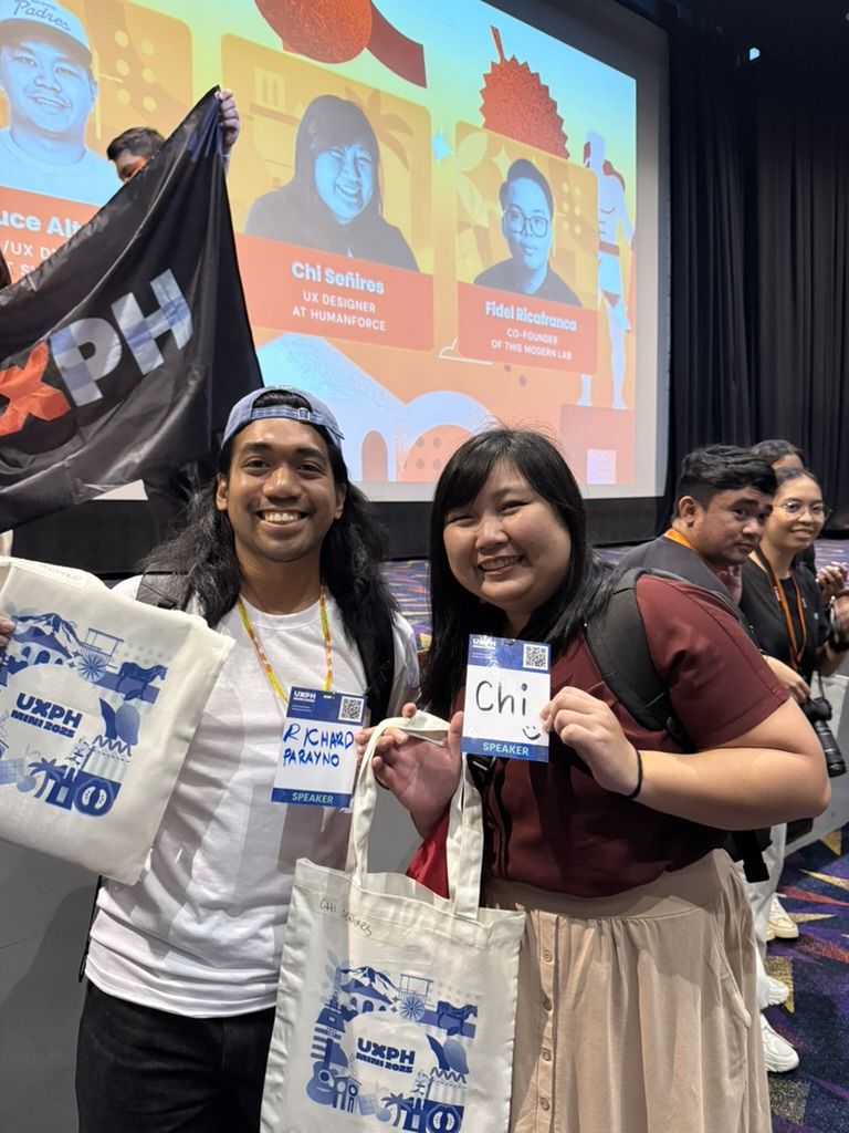 Richard joined in Cebu as a workshop facilitator too yayyy Richard and Chi posing near the stage for UXPH Mini 2025: Cebu, with both of them holding up their conference ID tags and their swag bags with the UXPH Mini branding printed on it.