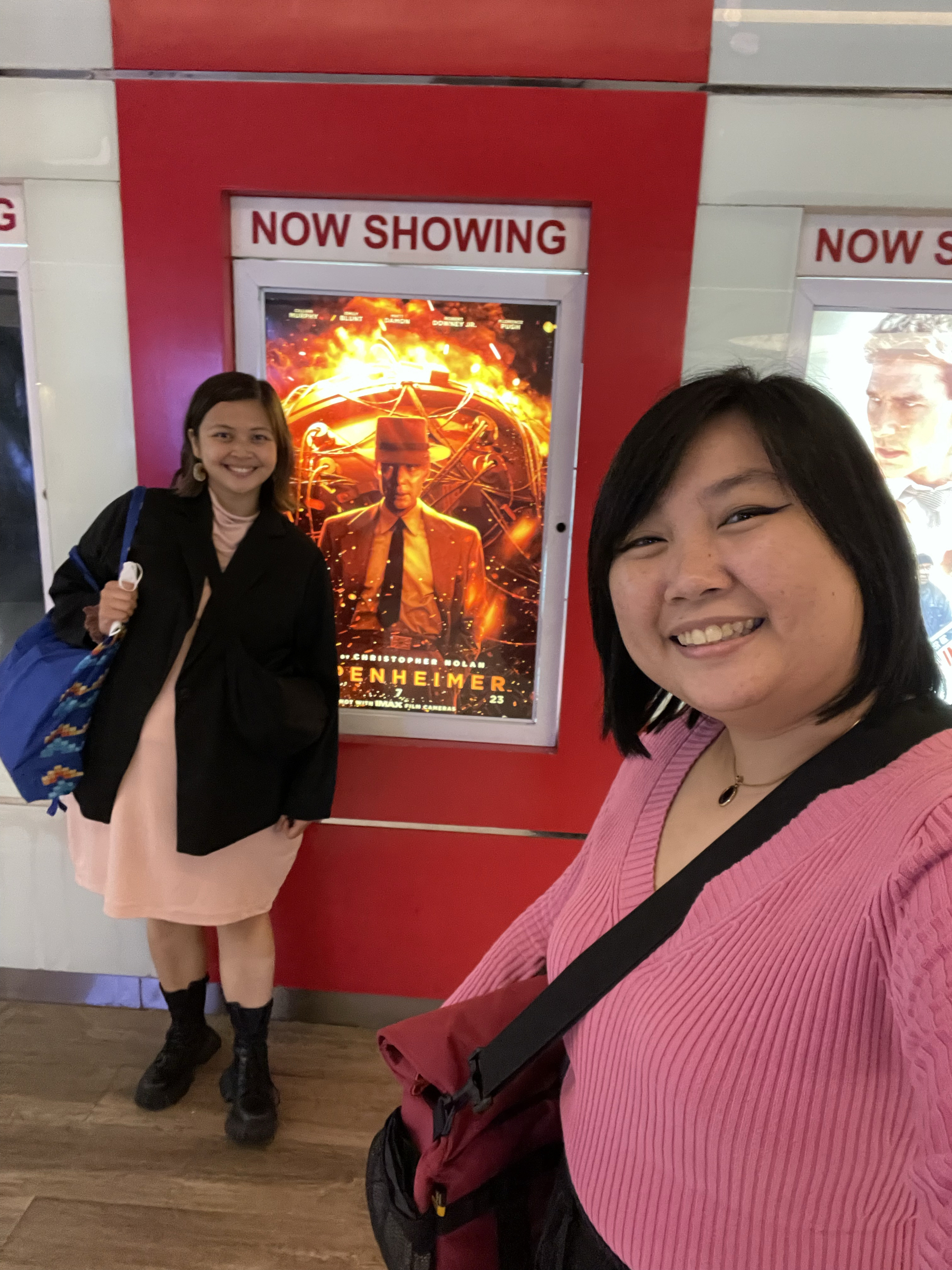 Karen and Chi posing next to the Oppenheimer movie poster.