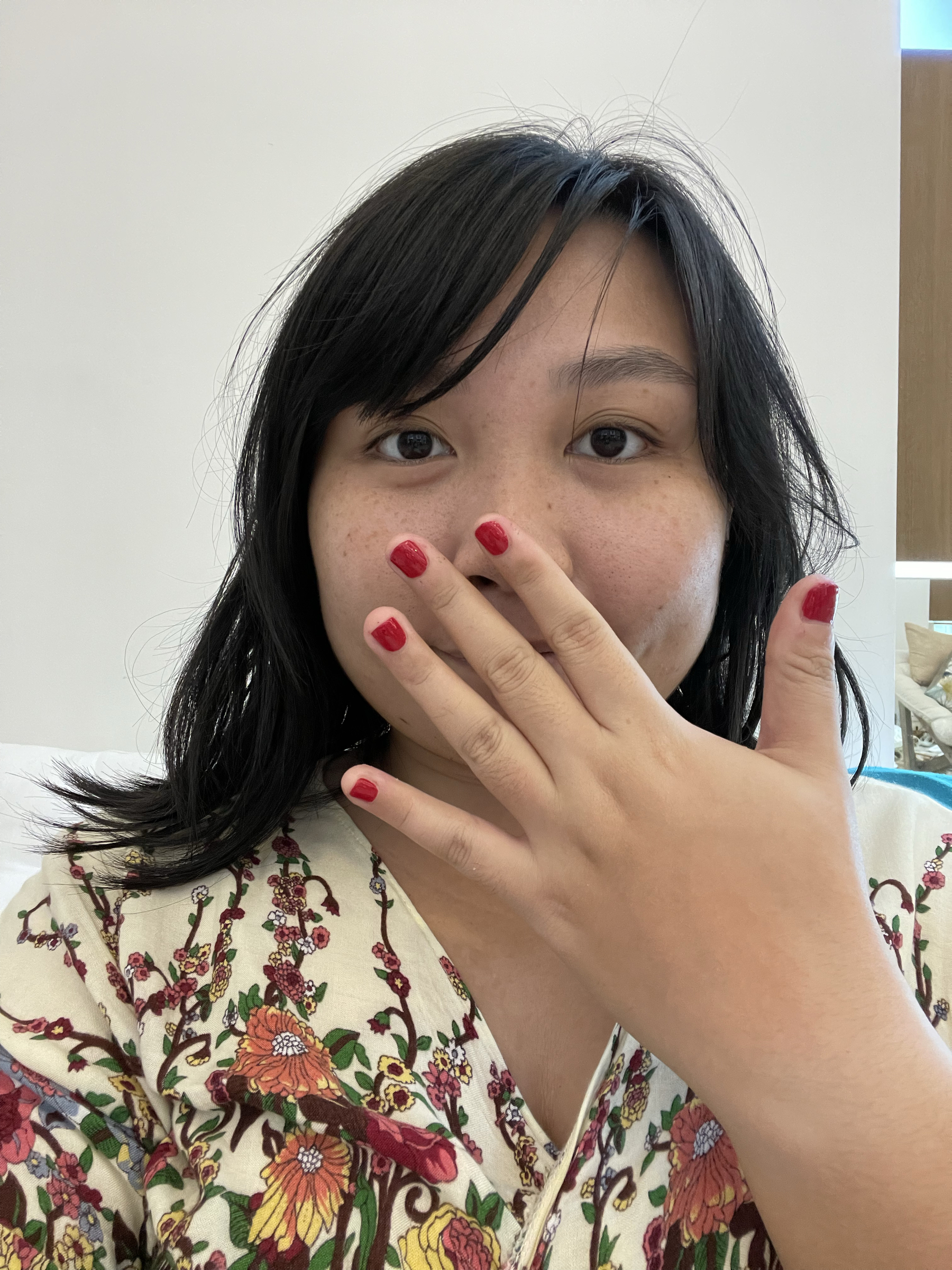 Chi holding her left hand up to cover her mouth, while extending her fingers more to show off her newly polished red nails from her manicure.