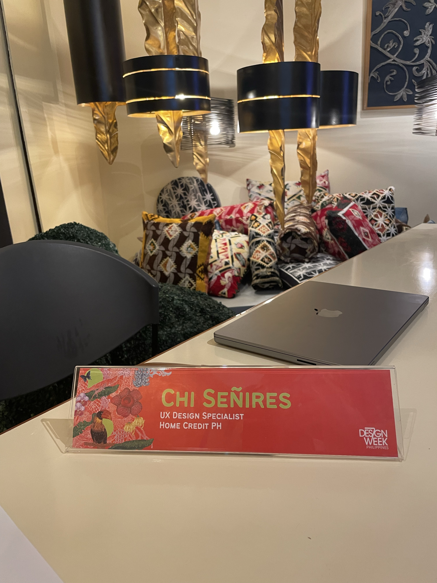 Chi’s name plate and placed on a table with her laptop behind it. The text on her name plate reads: “Chi Señires, UX Design Specialist, Home Credit PH”